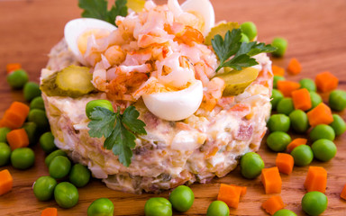 Olivier salad with shrimp, pickled cucumber, egg, decor of boiled carrots and peas on a wooden tray, board, dish, background
