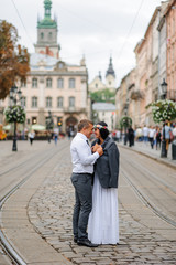 Fototapeta premium Wedding photo session In the center of the old city. The groom gave his bride his jacket so that she would warm herself. The couple hugs and smiles at each other. Rustic style wedding photography