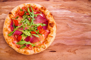 Pizza with ham, tomatoes, arugula on a wooden background