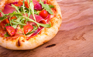 Pizza with ham, tomatoes, arugula on a wooden background