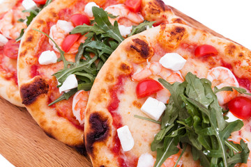 Three pizzas with prawns, tomatoes, arugula and cheese on a wooden background.