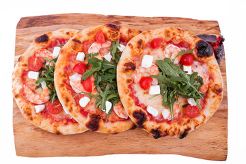 Three pizzas with prawns, tomatoes, arugula and cheese on a wooden tray. The object is isolated on a white background.