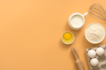 A variety of ingredients for baking on a pastel yellow background. Flour, eggs, milk, whisk and rolling pin. Top view, flat lay, copy space.