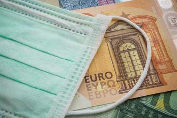 Obraz premium Face mask on Euro banknotes bill background. Global novel coronavirus (Covid-19) outbreak effect to EU, world economy, financial crisis, investment, stock market. Coronavirus pandemic in Europe.