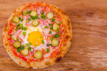 Pizza with ham, egg, pickled cucumber on a wooden background