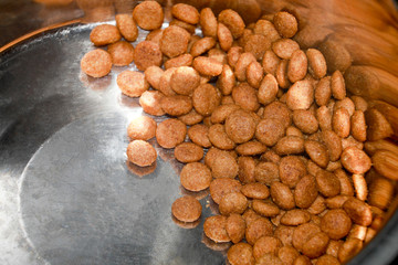 Close up dry crisp dog food in the stainless bowl background. Pets food concept.