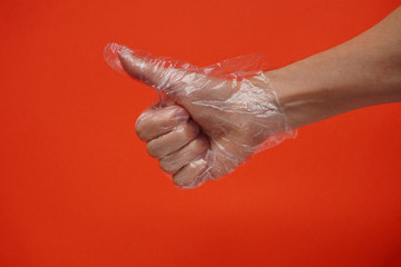 One hand in plastic or rubber protective disposable gloves on red background. Protection against viruses and bacteria during coronavirus pandemic.Thumbs up sign, copy space, ok or like sign concept