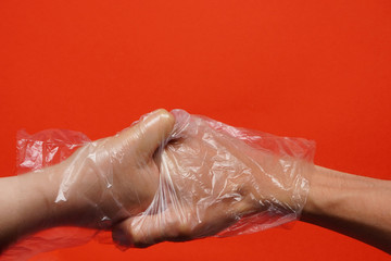 Handshake of man and woman on red background, hands in disposable transparent plastic or rubber gloves. Communication after coronavirus pandemic, distancing, protecting hand from viruses and bacteria