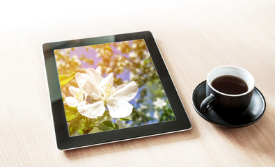 Tablet pc with spring flowers picture in screen, and a cup of coffee on the desk with sun light flash effect