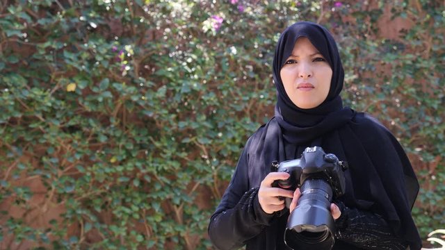 A beautiful Moroccan Arab Muslim woman with a DSLR camera taking pictures in a garden. Islamic emancipation. Real-time footage.