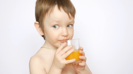 A beautiful naked boy drinks fresh orange juice from a glass