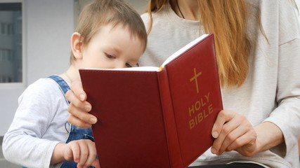 A beautiful woman reads the Holy Bible for her little son