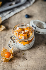  pudding with chia seeds in jars with mango slices and pine nuts on shabby beige background, healthy breakfast concept