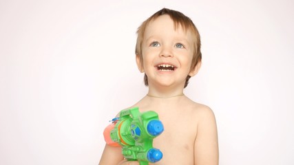 A happy little boy with a water gun looks up smiling