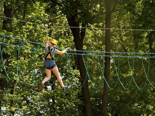 Yaslo, Poland - 8 7 2019:A young girl climbs the trees in gear in a park for rock climbing. Scandinavian attraction for sports events. Rope insurance and means of protection. Safety at altitude