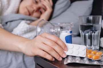 young sick woman in bed drinks pills