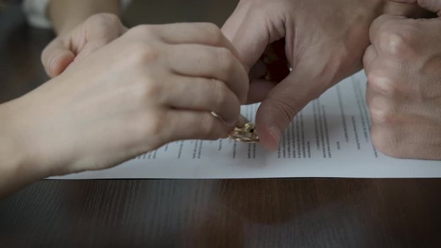 Paper of end of love. A man and a woman take off their wedding rings from divorce papers.
