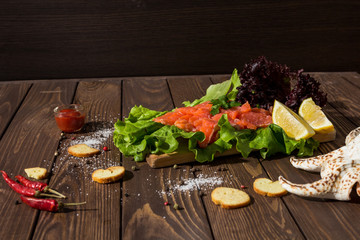slices of red fish fillet on a wooden background. trout, lettuce, crackers, toasts, red pepper. preparing breakfast