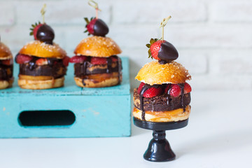 Sweet burger with vanilla bun, brownie layer, strawberries in chocolate and salted caramel. White background.