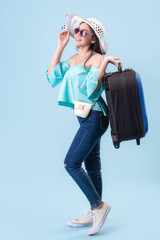 A young Asian girl with a bright face, wearing a hat and wearing glasses. Holding luggage to travel in summer in studio Blue pastel background. Pastel Blue tone filters.