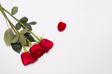 Three red roses flat lay on white background with copy space. Velvet box for jewelry shaped heart near.