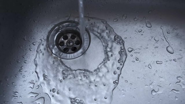 wasting of water. water from tap running flows down on the stainless kitchen sink drain. concept of conservation and reducing unnecessary water usage when staying at home.