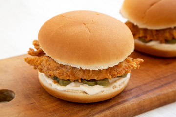Homemade Burgers with fried chicken strips on a rustic wooden board on a white wooden surface, low angle view. Close-up.
