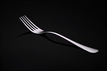 A white metal fork rests on a black glass.