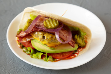 Homemade Bacon Cheeseburger Taco on a white plate on a gray surface, side view. Close-up.