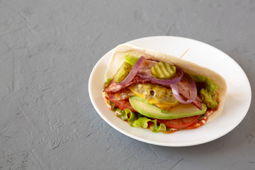 Homemade Bacon Cheeseburger Taco on a white plate on a gray background, side view. Space for text.