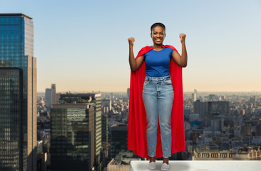 Fototapeta na wymiar women's power and people concept - happy african american woman in red superhero cape over tokyo city skyscrapers on background
