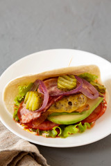 Homemade Bacon Cheeseburger Taco on a white plate on a gray background, side view. Space for text.