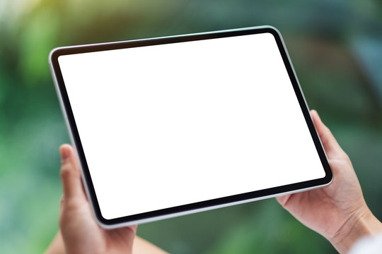 Mockup image of a woman holding black tablet pc with blank white desktop screen , green nature background