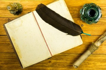 Inkwell from green glass, open book, document in a scroll, feather and candle on a wooden background.