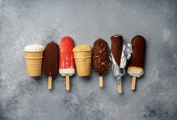 Chocolate ice cream popsicles and fruit ice cream with cones on gray cold stone background. Copy...