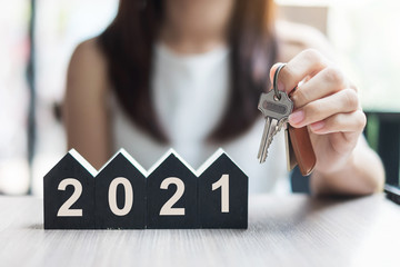 Young Businesswoman hands holding key and 2021 Happy New Year with house model on table office. New House, Financial, Property insurance, real estate, savings and New Year Resolution concepts