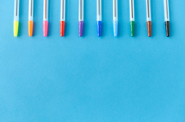 school, writing tools and object concept - row of many multicolored pens on blue background