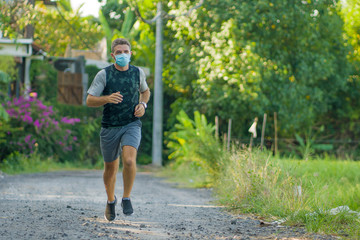 Fototapeta premium covid-19 deconfinement - young attractive and happy man outdoors in city park doing running workout wearing protective face mask jogging and training after quarantine