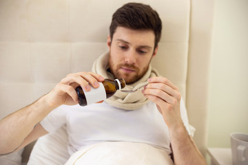 Man Drinking Cough Syrup in Bed. Sick Man at Home Staying in Bed. Self Treatment