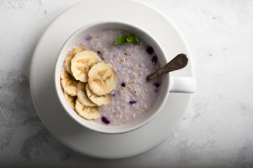 Top view image of oatmeal porridge with berries, bananas and mint leaves. Healthy vegetarian breakfast concept