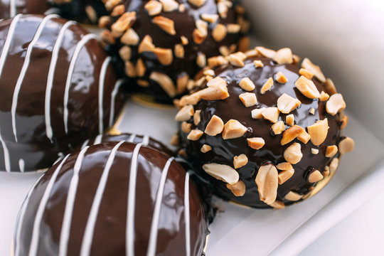 Chocolate covered Bavarian cream donut topping with crush peanuts in paper box. Tasty dessert pastry.