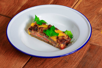 Homemade meat casserole with mushrooms and tomatoes and fresh pardley served on white plate over wooden background.