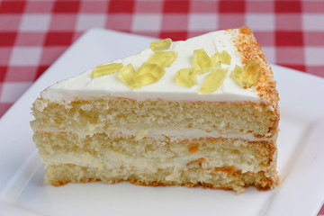 A piece of lemon sponge cake with cream served on a white plate over red plaid tablecloth. Italian concept.