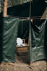 A self-built outhouse with toilet seat and tarpaulin outdoor in the forest in the nature
