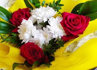Beautiful bouquets of white chrysanthemums and red roses with green leaves in yellow packaging
