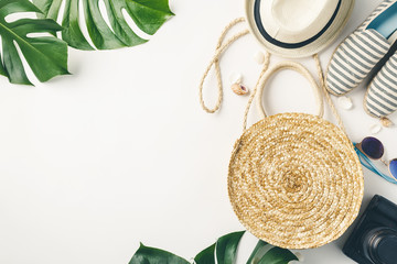 Straw hat, camera, bag, summer shoes, sunglasses, shells and tropical leaves over white background, top view.