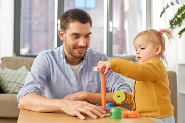Obraz premium family, fatherhood and people concept - happy father and little baby daughter playing with pyramid toy at home
