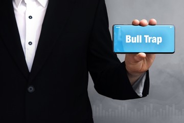 Bull Trap. Geschäftsmann im Anzug hält ein Smartphone in die Kamera. Der Begriff Bull Trap steht auf dem Handy. Konzept für Business, Finanzen, Statistik, Analyse, Wirtschaft