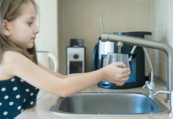 Child is holding a transparent glass. Filling cup beverage. Pouring fresh drink. Consumption of tap...