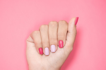 Closeup top view flatlay photography of one beautiful manicured female hand isolated on pink background. Woman with trendy colorful two colours modern nail design of bright pink and purple colors.